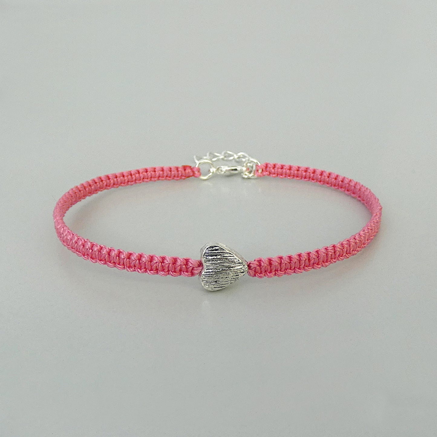Pink seven inch macramé bracelet with silver plated textured heart charm, lobster clasp and one inch extender chain.