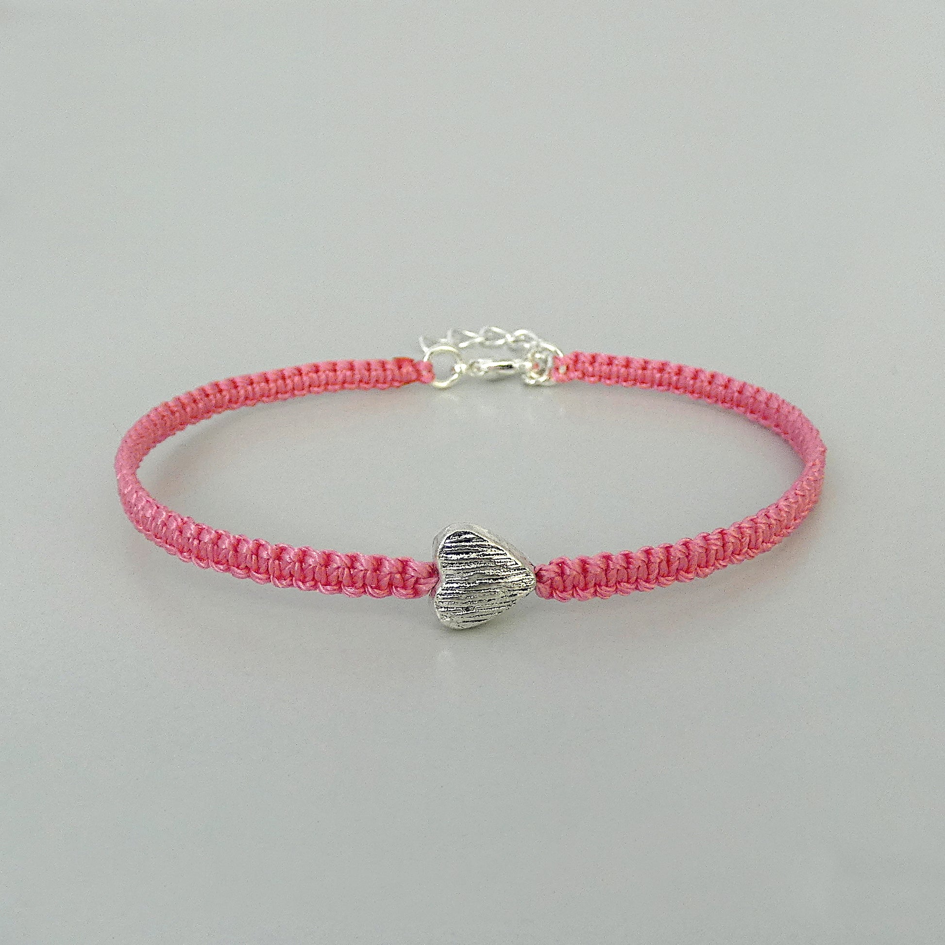 Pink seven inch macramé bracelet with silver plated textured heart charm, lobster clasp and one inch extender chain.