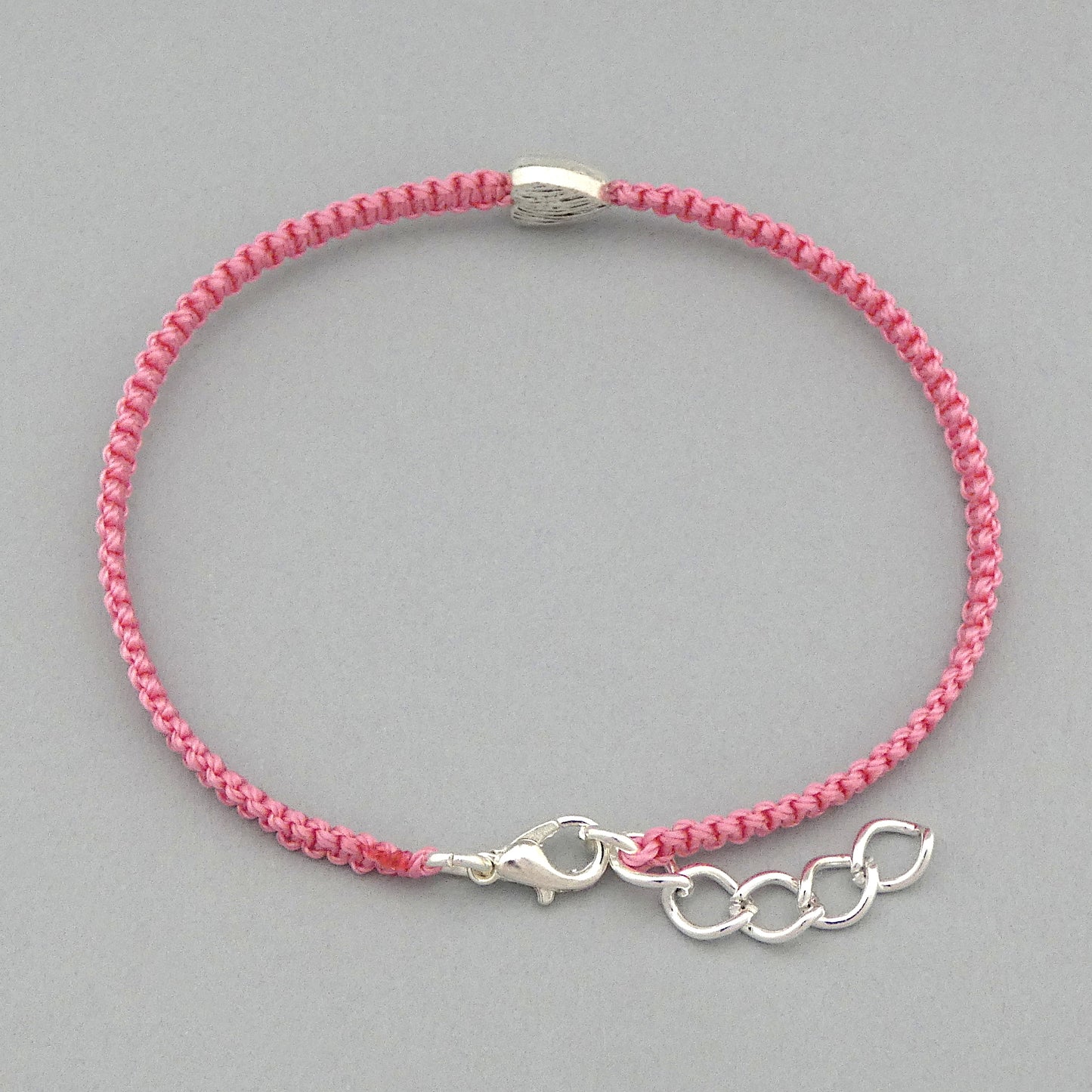 Silver plated lobster claw clasp and one inch extender chain on a pink seven inch macramé bracelet with silver plated textured heart charm.