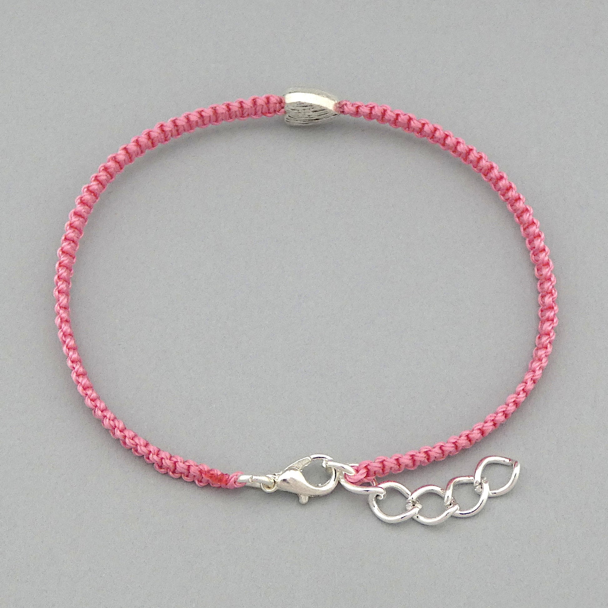 Silver plated lobster claw clasp and one inch extender chain on a pink seven inch macramé bracelet with silver plated textured heart charm.