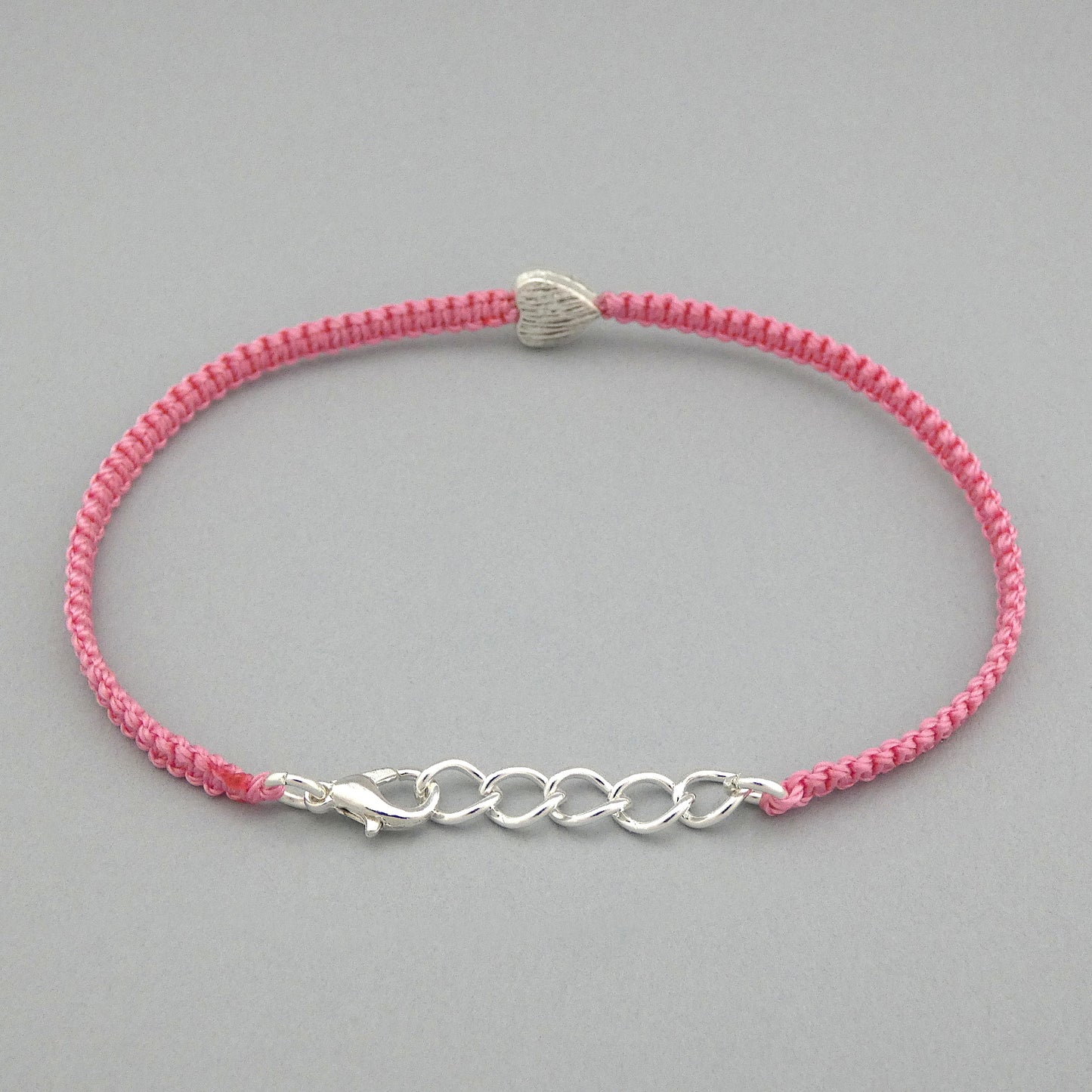 Silver plated lobster claw clasp attached to the end of a one inch extender chain on a pink seven inch macramé bracelet with silver plated textured heart charm.
