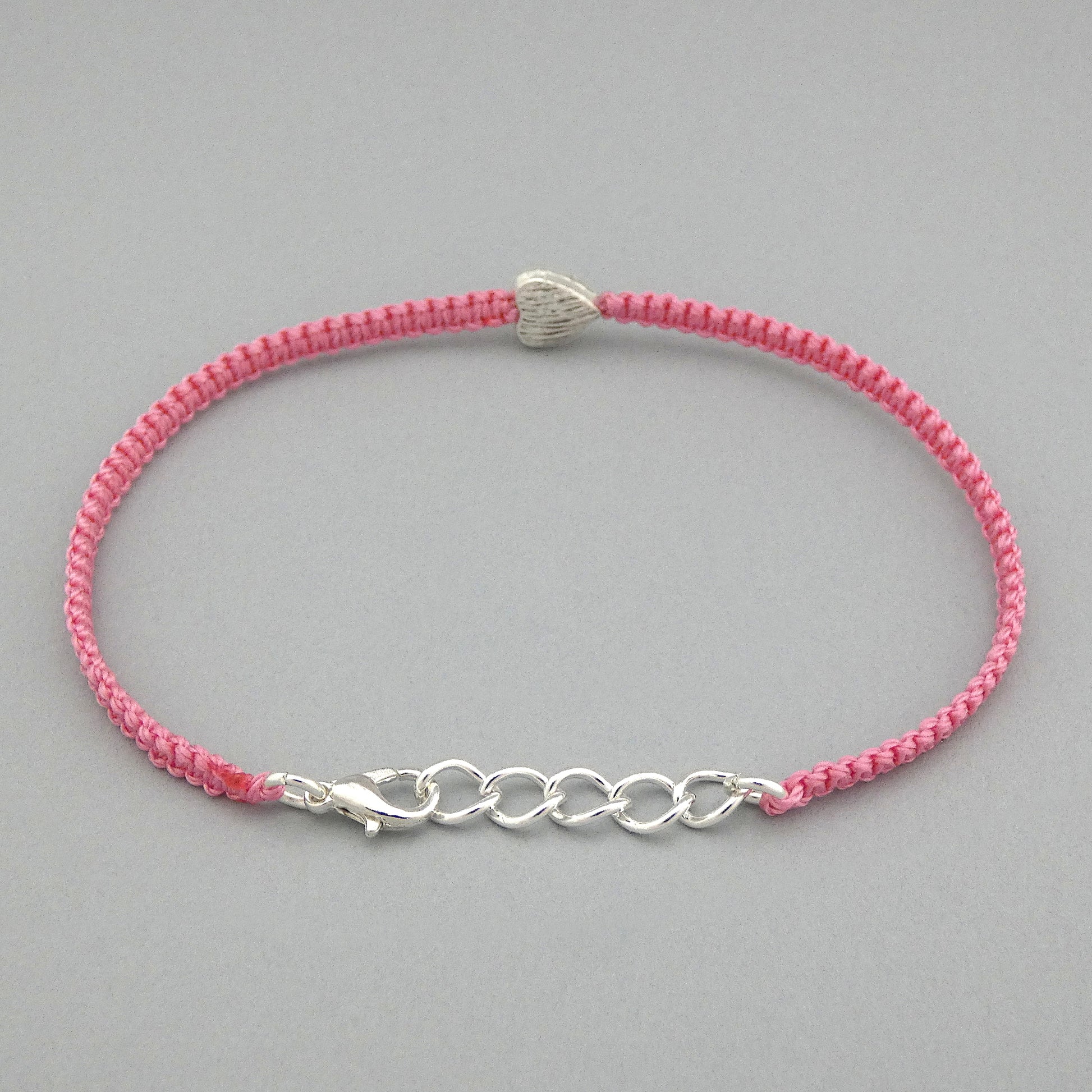 Silver plated lobster claw clasp attached to the end of a one inch extender chain on a pink seven inch macramé bracelet with silver plated textured heart charm.