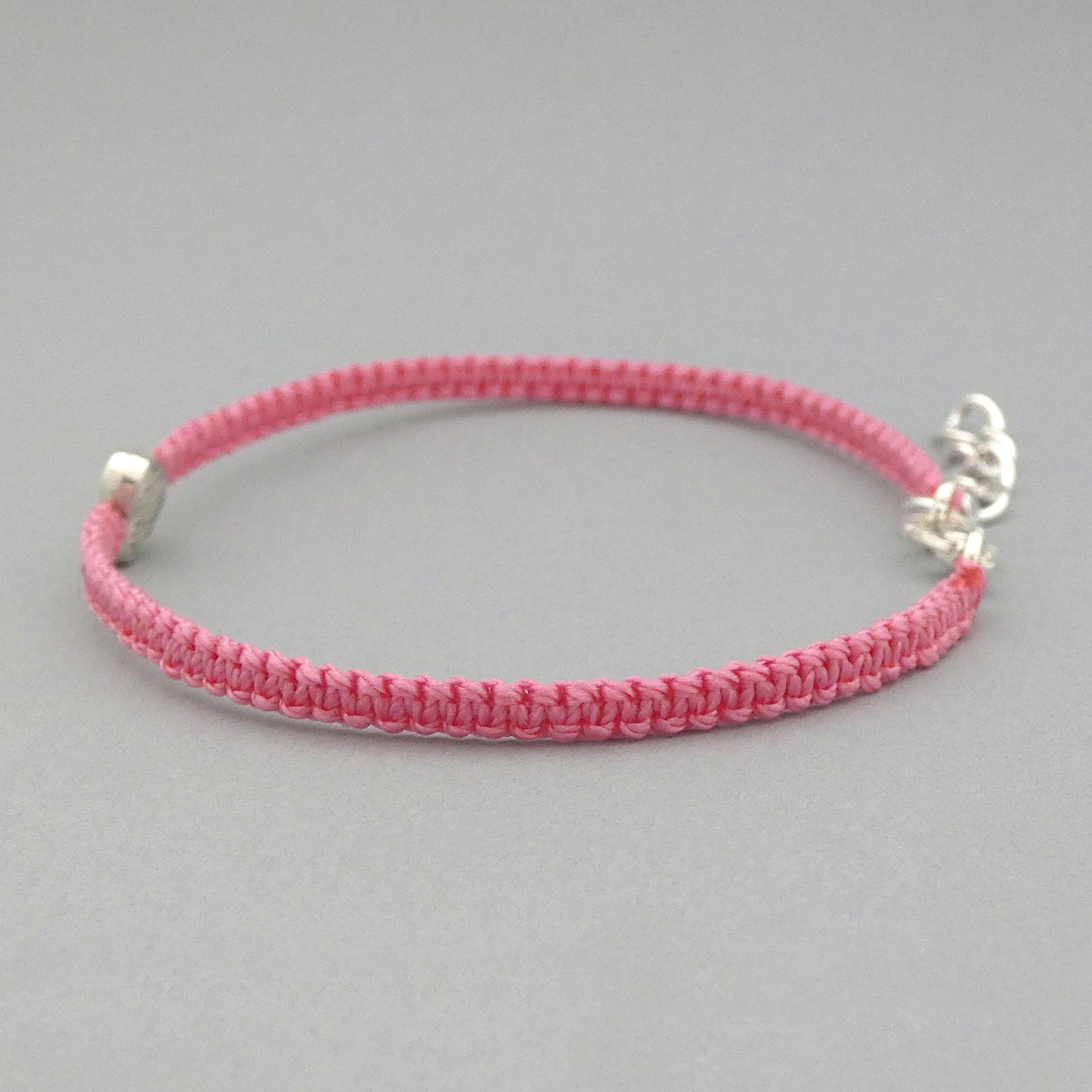 Side view of knots on a pink seven inch macramé bracelet with silver plated textured heart charm.