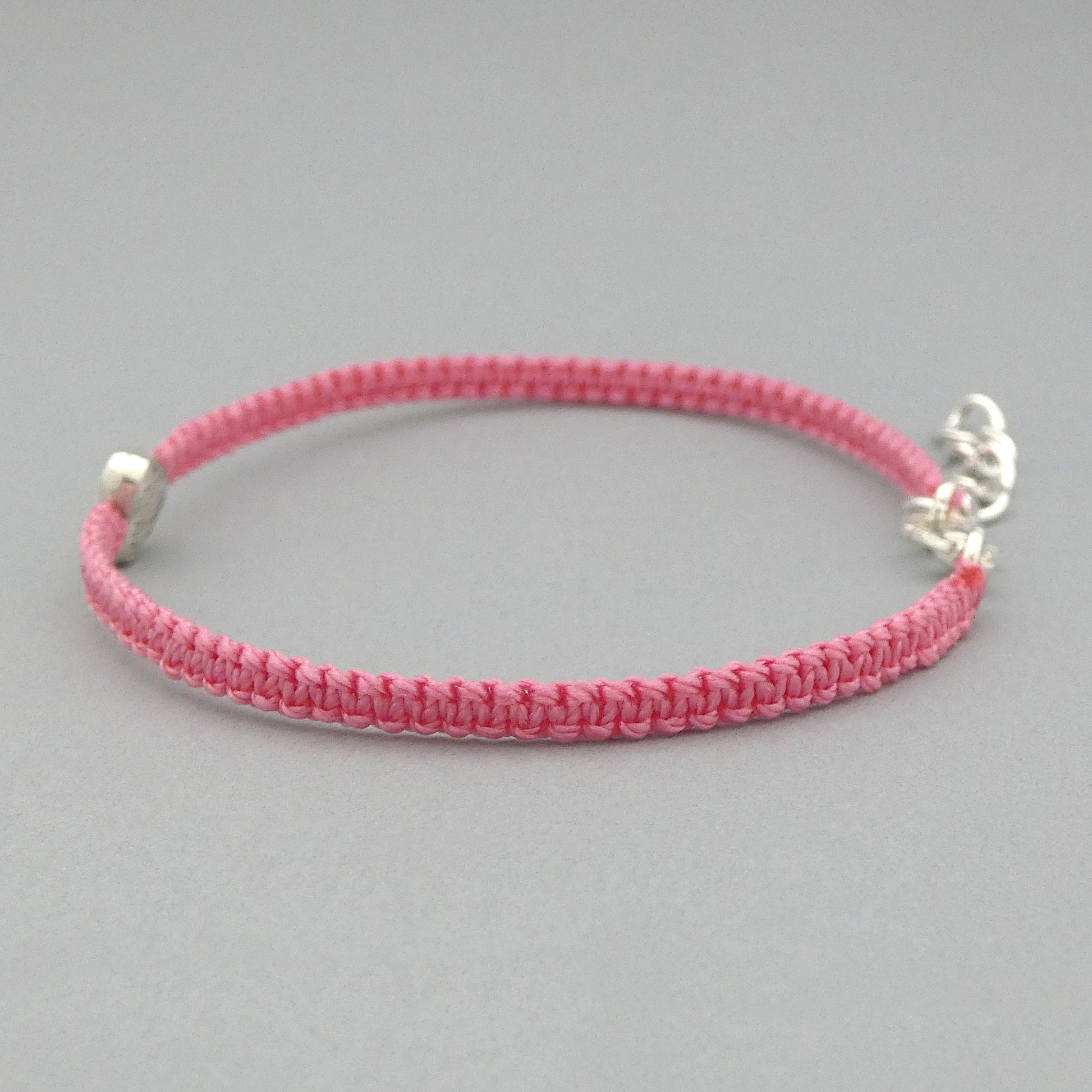 Side view of knots on a pink seven inch macramé bracelet with silver plated textured heart charm.